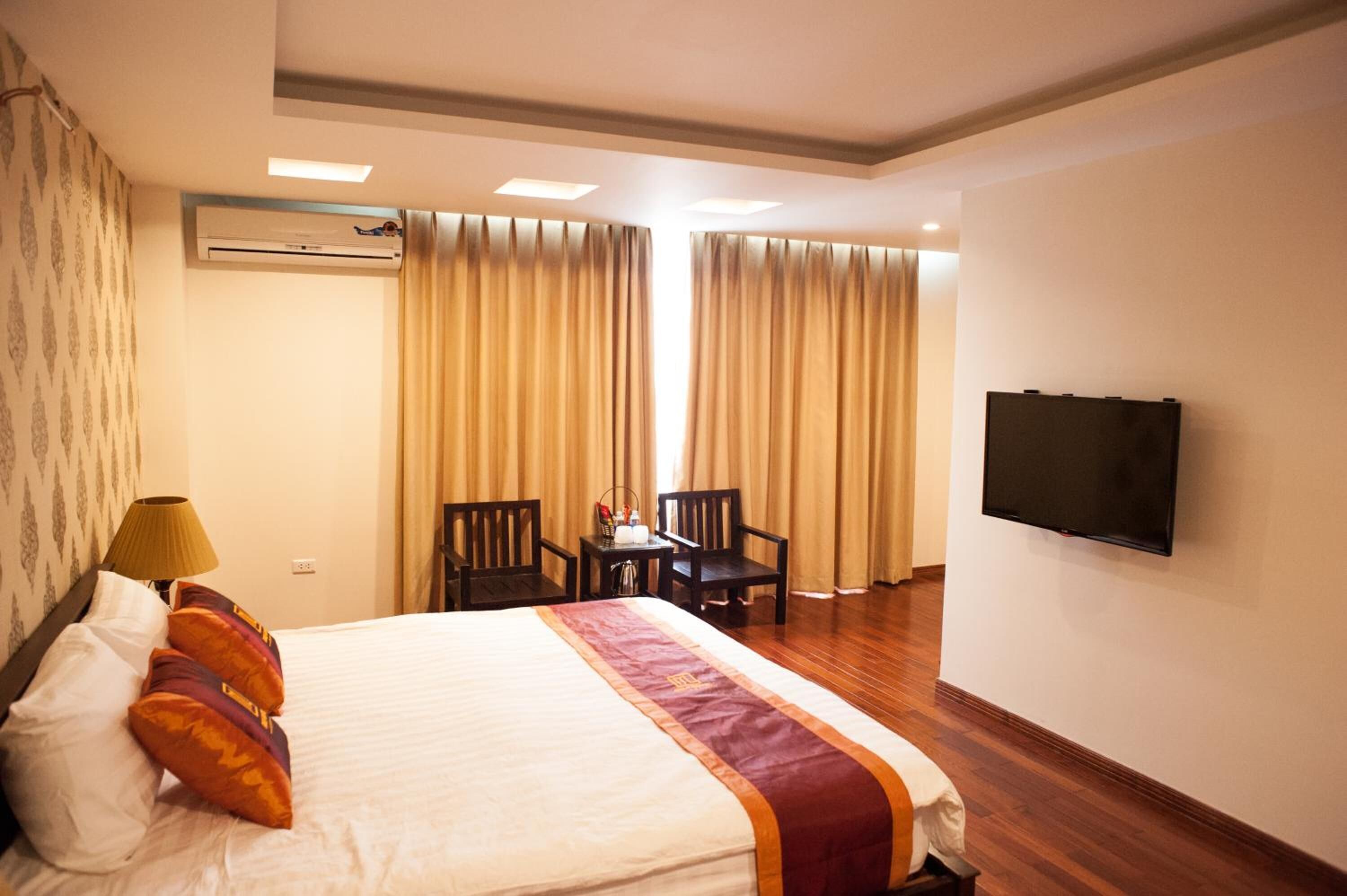 A hotel room with a bed, a desk with chairs, a television, and curtains.