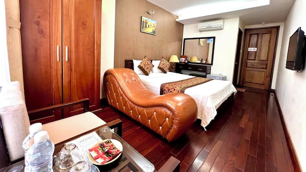 A hotel room with a large bed, a leather armchair, a desk with a water bottle and snacks, and a TV. - Mely Hotel (Hanoi)