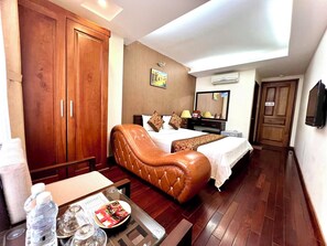 A hotel room with a large bed, a leather armchair, a desk with a water bottle and snacks, and a TV. - Mely Hotel (Hanoi)