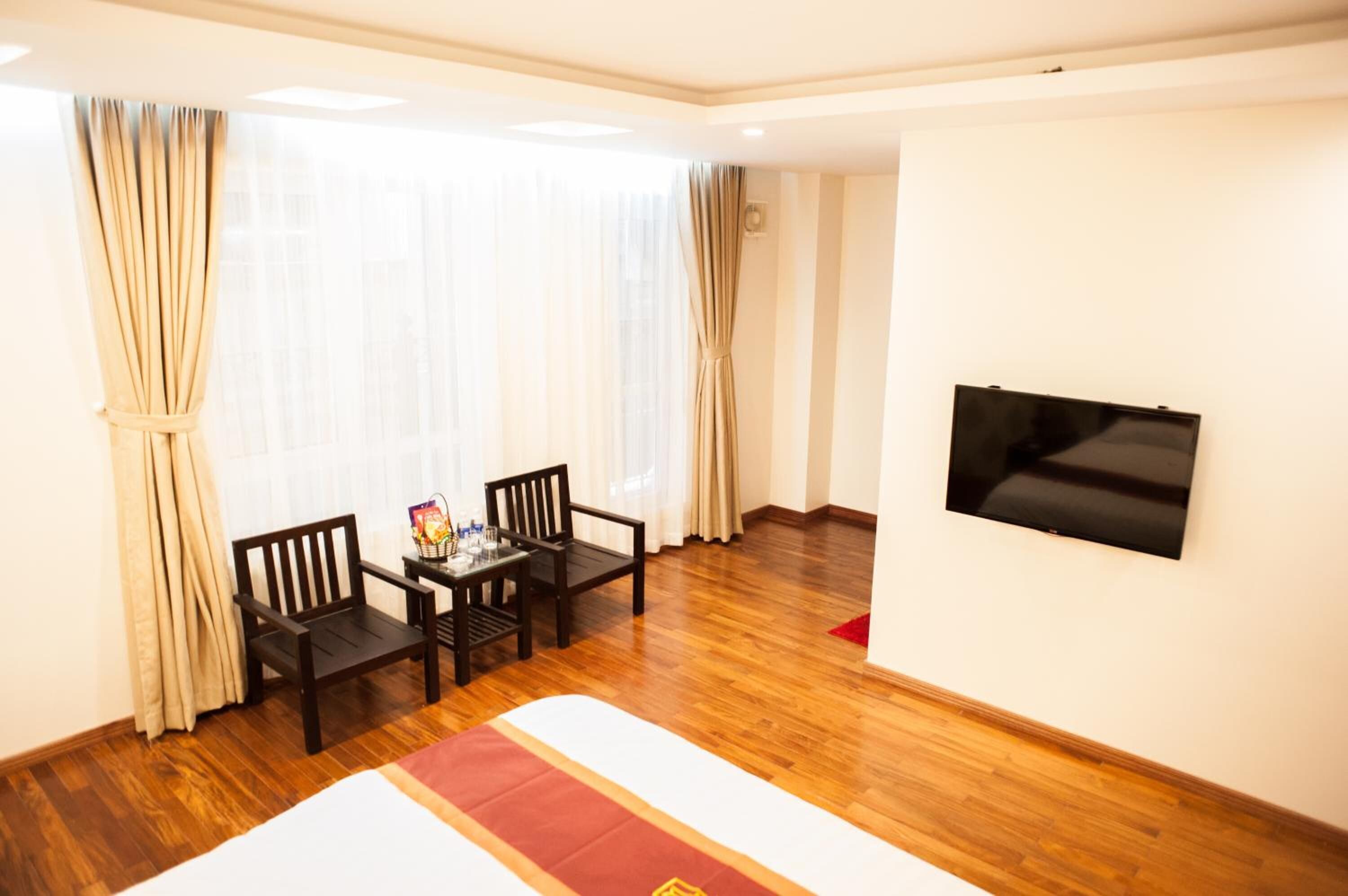 Quarto de hotel com cama, piso de madeira, televisão fixada na parede e janela com cortinas.
