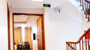 A hotel corridor with a carpeted floor, wooden doors, a staircase with a wooden railing, and a sign indicating an exit. - Mely Hotel (Hanoi)
