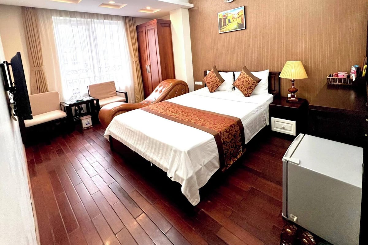 A hotel room with a large bed, a desk, a chair, a TV, and a window with curtains.