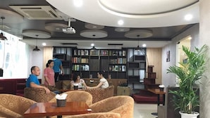 A modern library with sofas, a coffee table, and a bookshelf filled with books. - Mely Hotel (Hanoi)