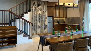 A modern kitchen with a built-in refrigerator, a dining area with a table set for four, and a staircase with wooden railings. - Putri Duyung Ancol (Jakarta)