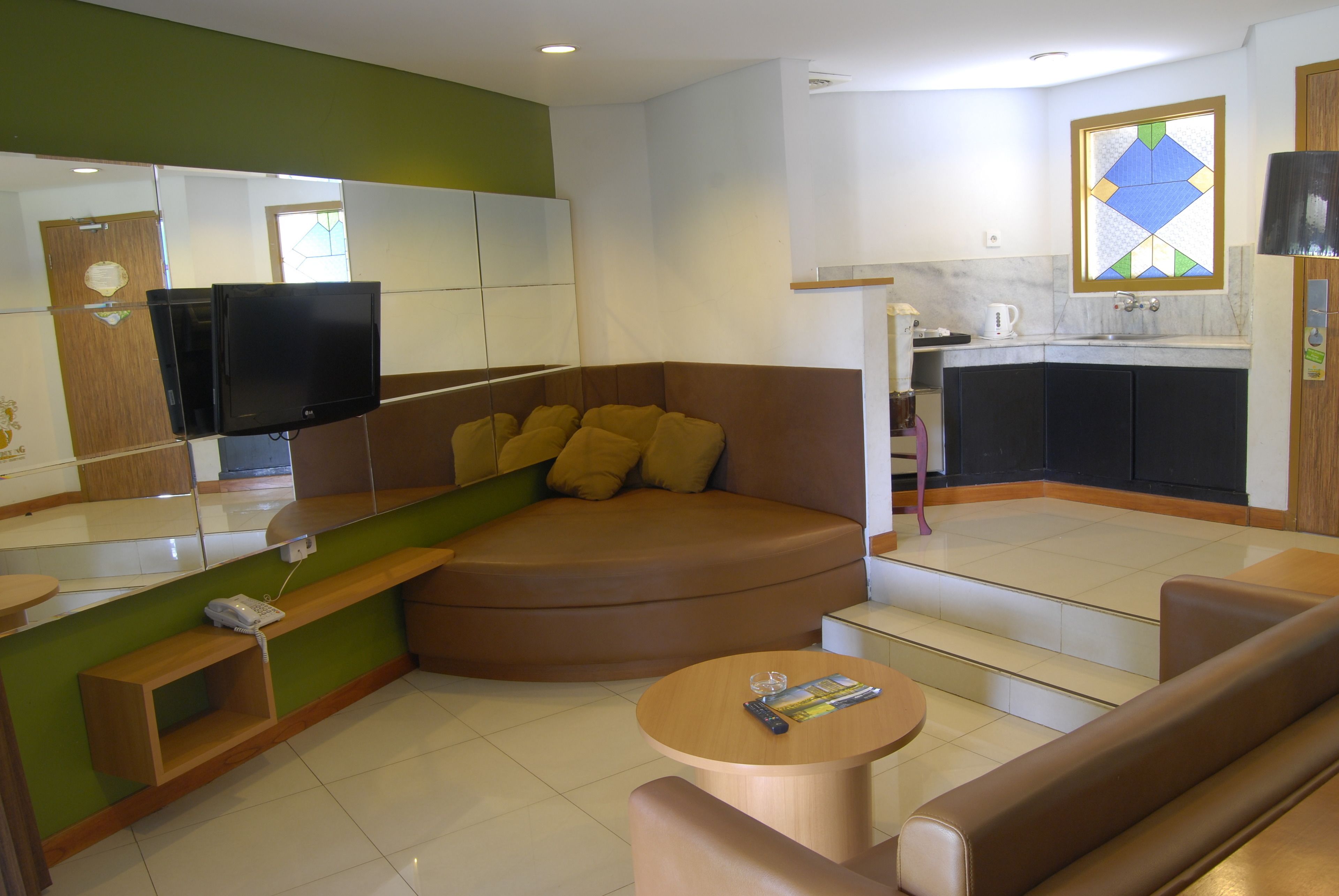 A modern living room with a brown sofa, a small round table, and a television mounted on a glass partition.