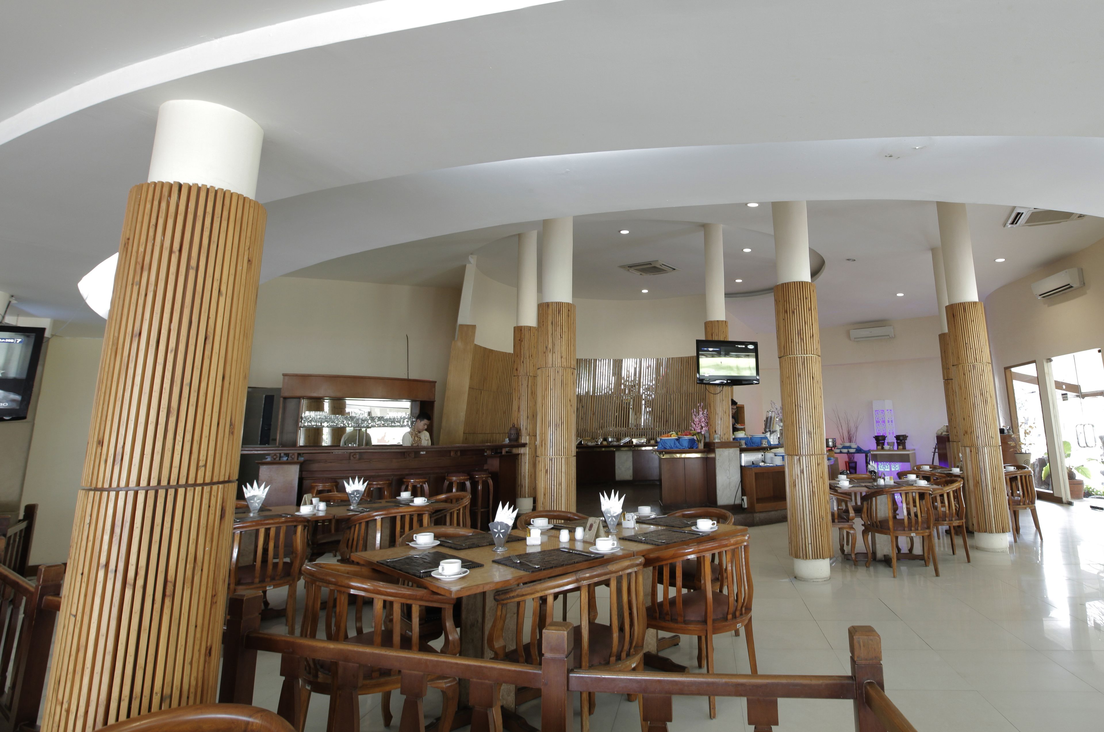 Un restaurant spacieux avec de hauts piliers en bois, de nombreuses tables et un décor intérieur moderne.