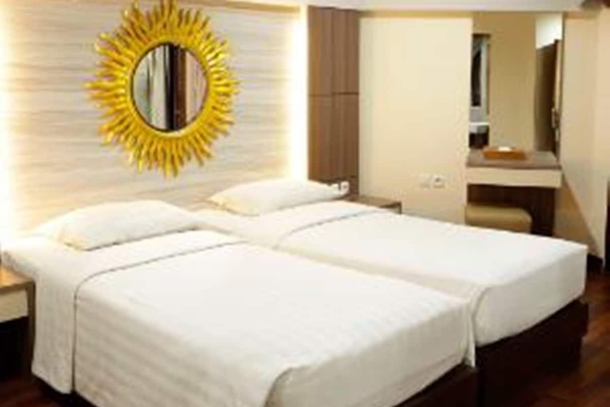 Une chambre d’hôtel avec un grand lit, une table de chevet, un miroir avec un cadre en forme de soleil et un plancher en bois.