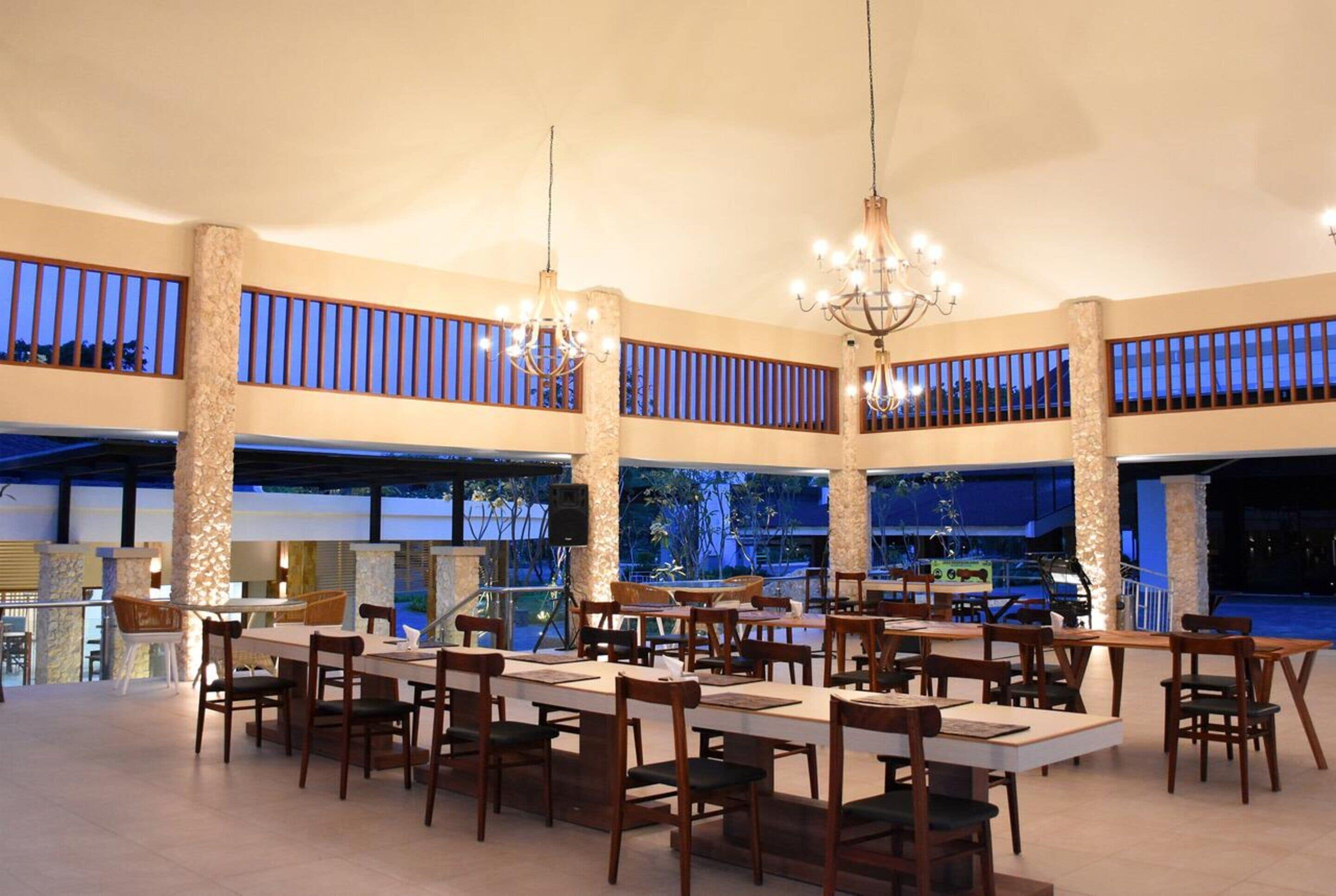 A spacious indoor dining area with multiple tables and chairs, large pillars, and a balcony with a railing.