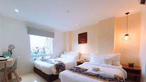 A hotel room with two beds, a desk, and a window with a view of buildings.