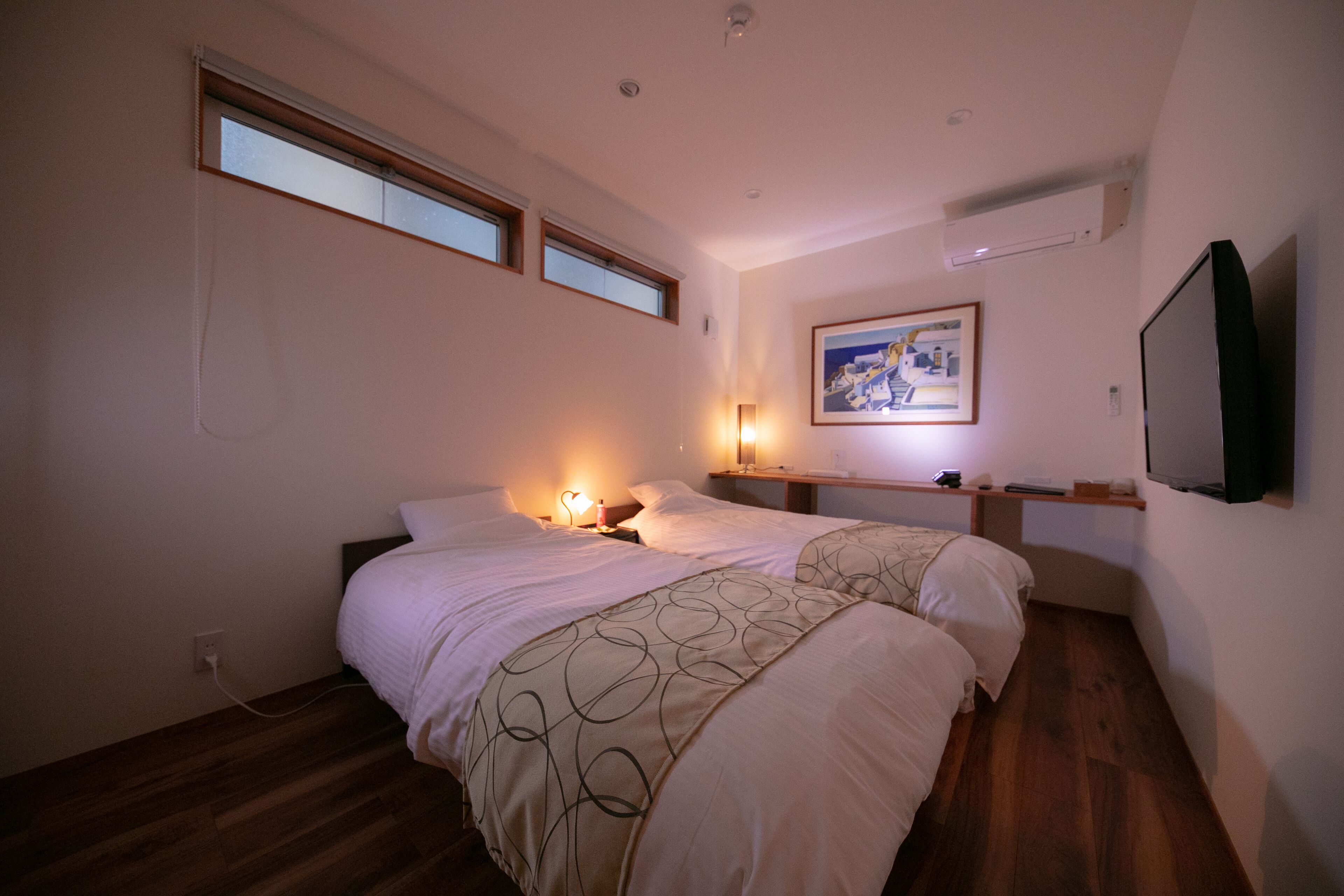 A bedroom with two beds, a nightstand, a wall-mounted TV, and a painting.