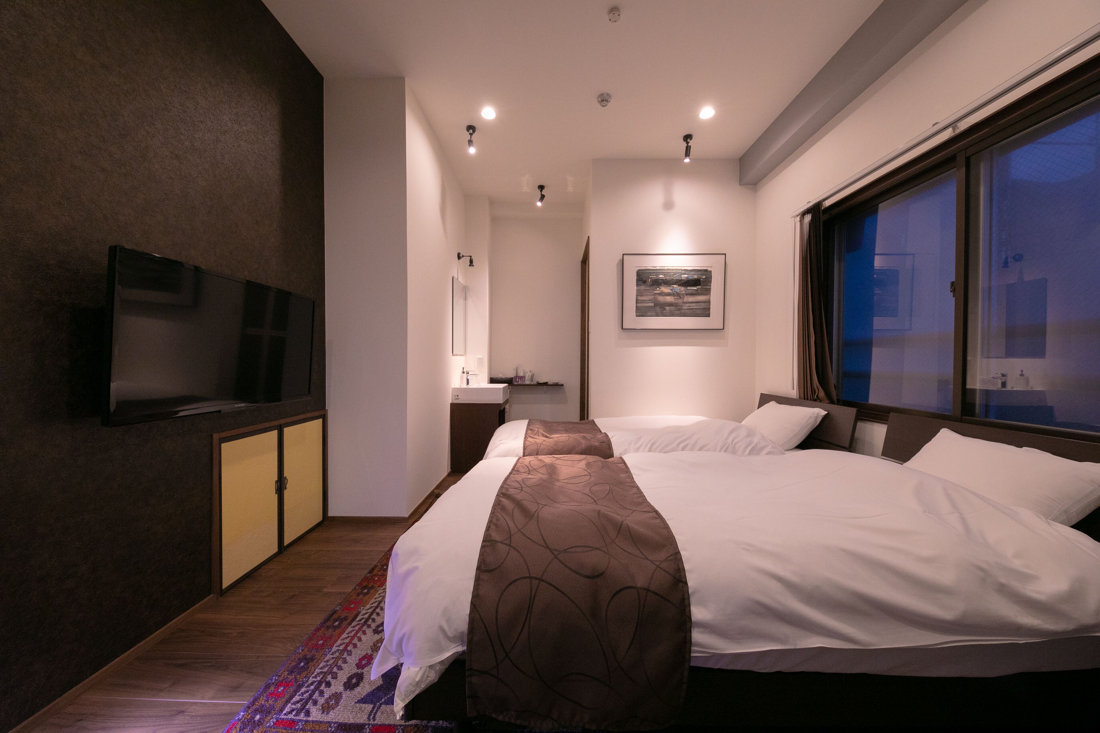 A modern hotel room with a large bed, a flat-screen TV mounted on the wall, and a window with a view of the city.