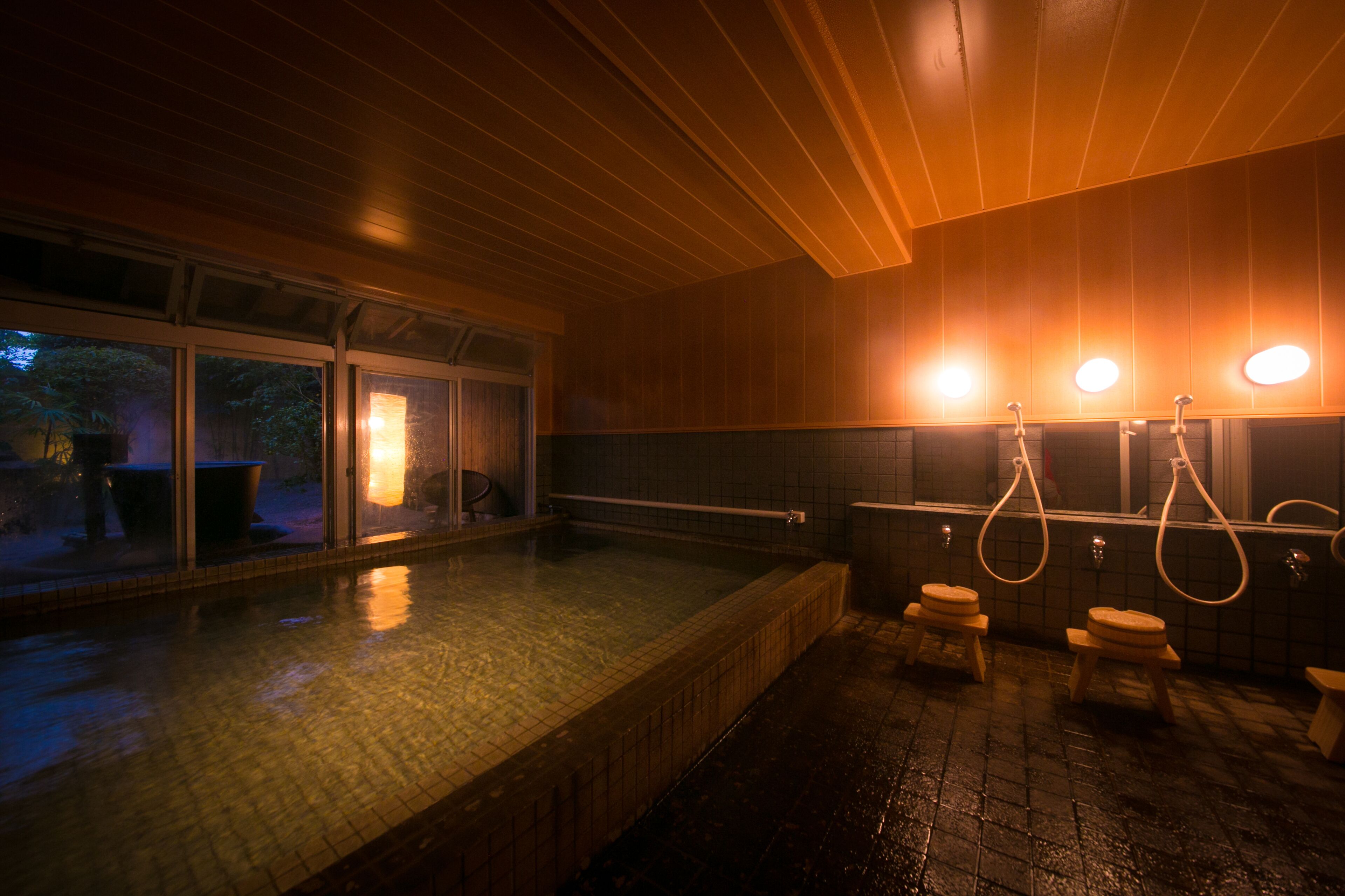 A traditional Japanese onsen with a wooden interior, a tiled floor, and a view of the outside through large windows.