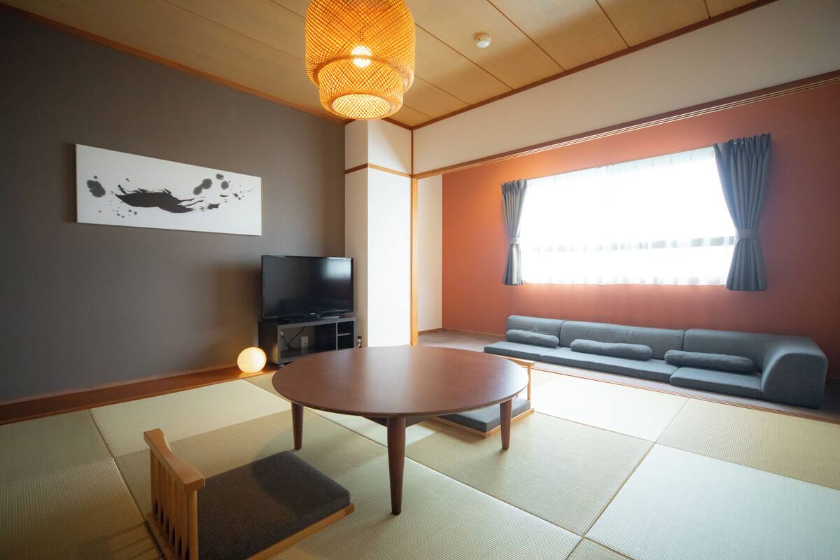 Un salón japonés tradicional con suelo de tatami, una mesa baja, un sofá y un televisor.