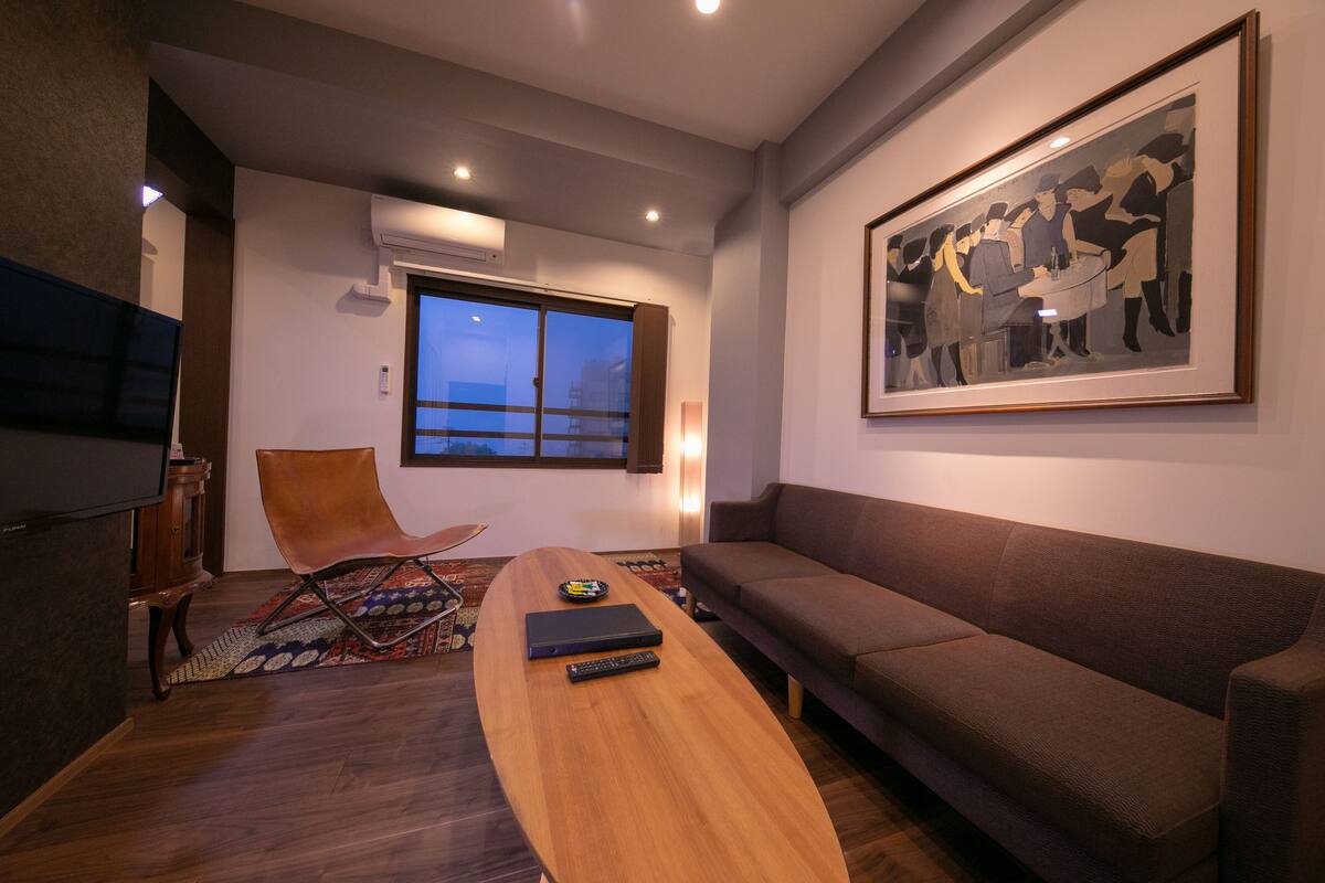 Una sala de estar moderna con una mesa de centro de madera, un sofá marrón, una obra de arte enmarcada en la pared y un ventanal grande.