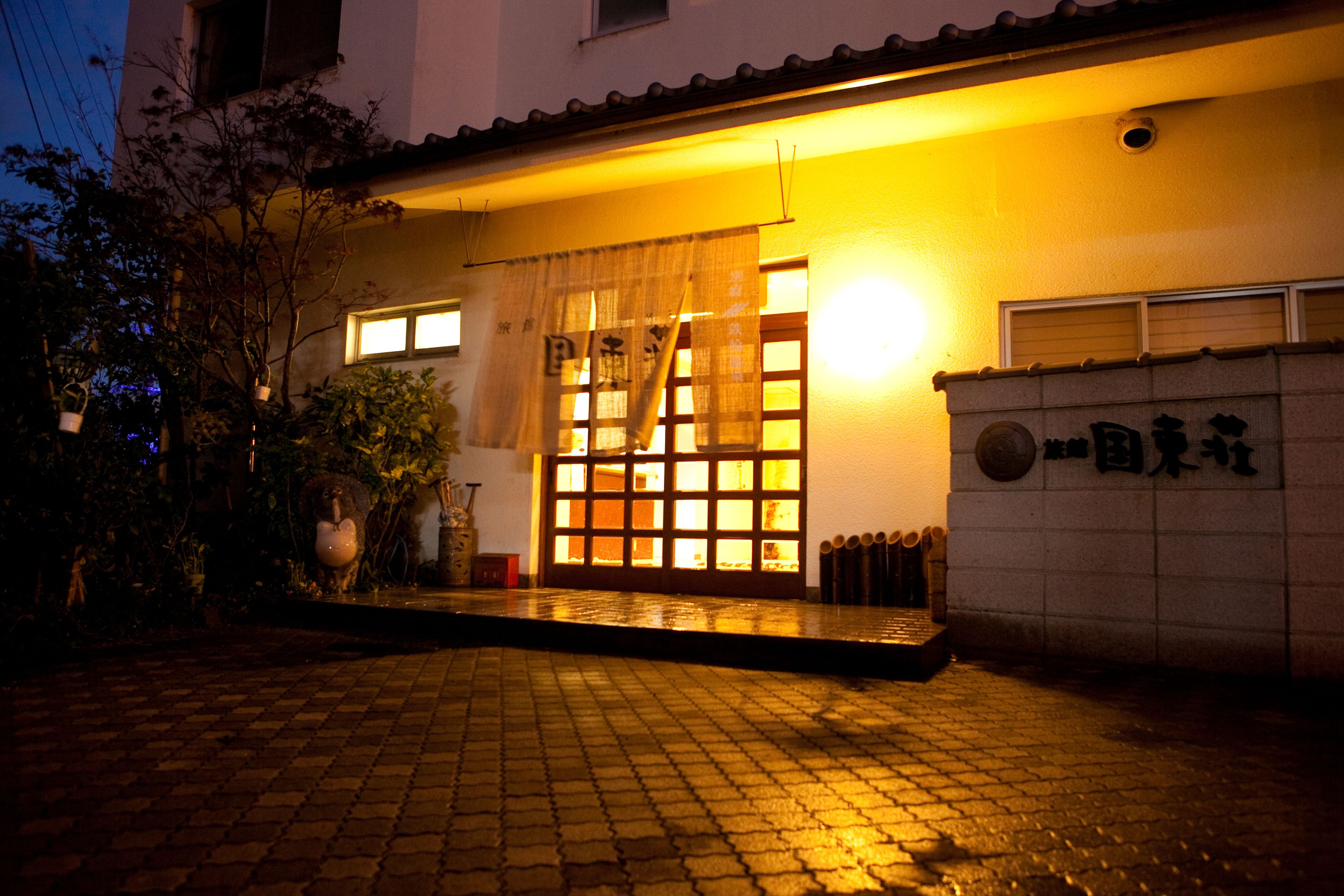 Un edificio japonés tradicional con un porche adoquinado, una puerta de madera y un letrero con caracteres japoneses.
