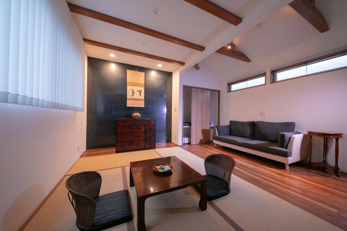 Una sala de estar moderna con un sofá, una mesa de comedor con sillas, un aparador de madera y un ventanal grande.