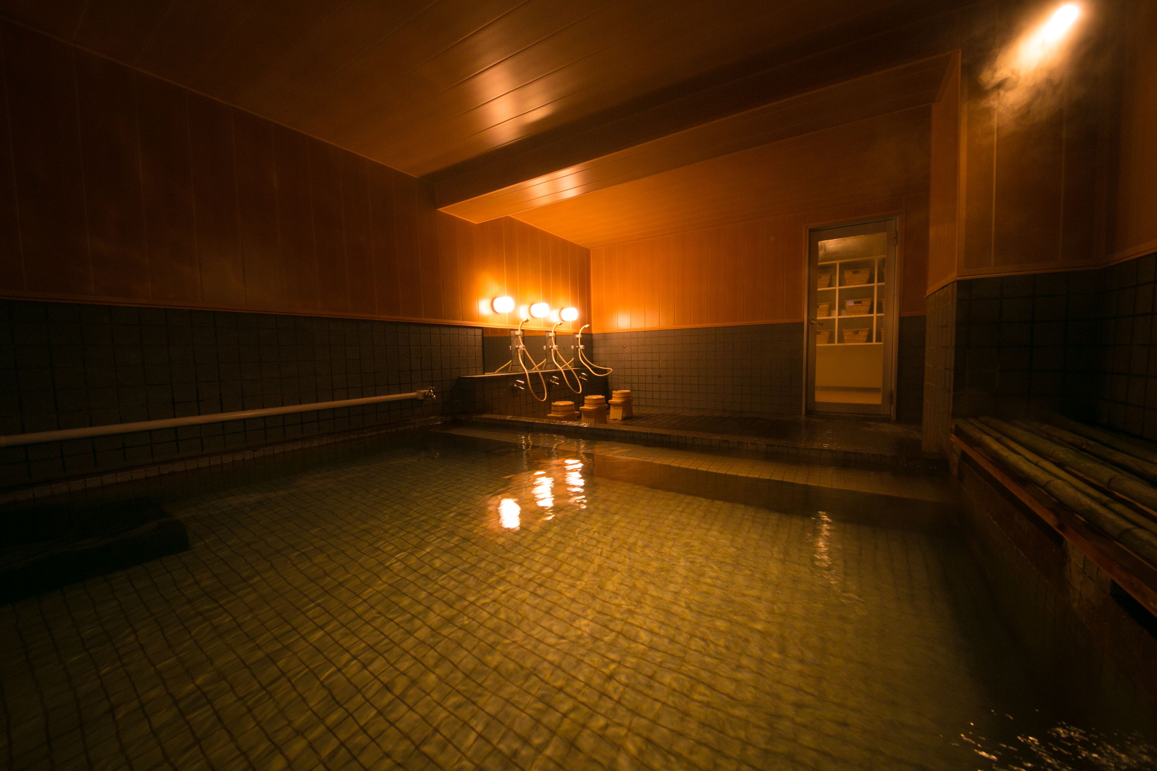 Una piscina coperta scarsamente illuminata, con pareti piastrellate e una panchina lungo il bordo.
