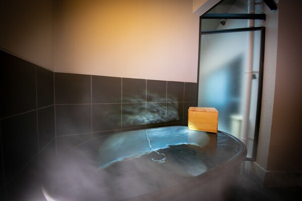 A hot tub with a wooden block, tiled walls, and a glass door.