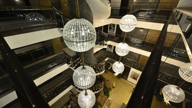 Een atrium met meerdere verdiepingen, moderne kroonluchters, glazen balustrades en een centraal zitgedeelte.