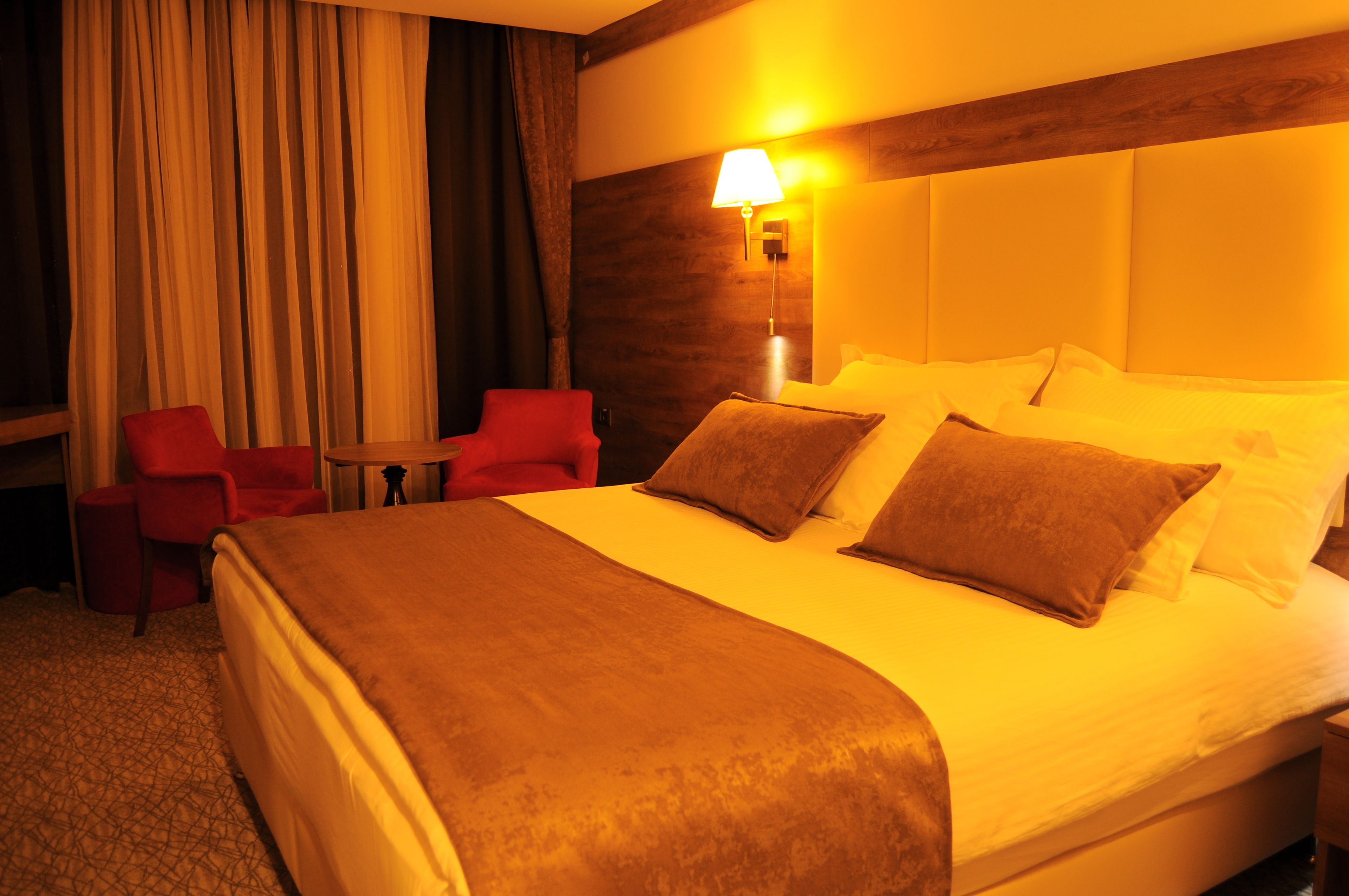 A hotel room with a large bed, red chairs, a small table, and a lamp.