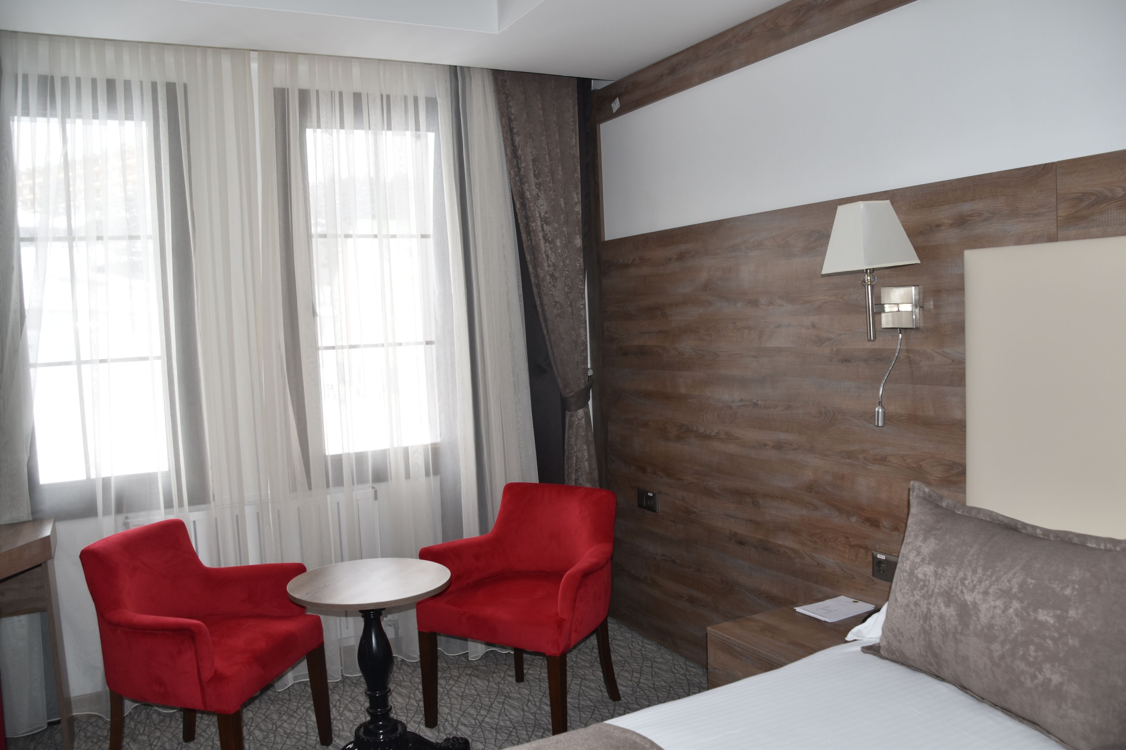 A hotel room with a bed, a red armchair, a round table, and a lamp.