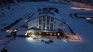 Een met sneeuw bedekt gebouw met een brede ingang, meerdere ramen en een bord waarop staat dat het een hotel is.
