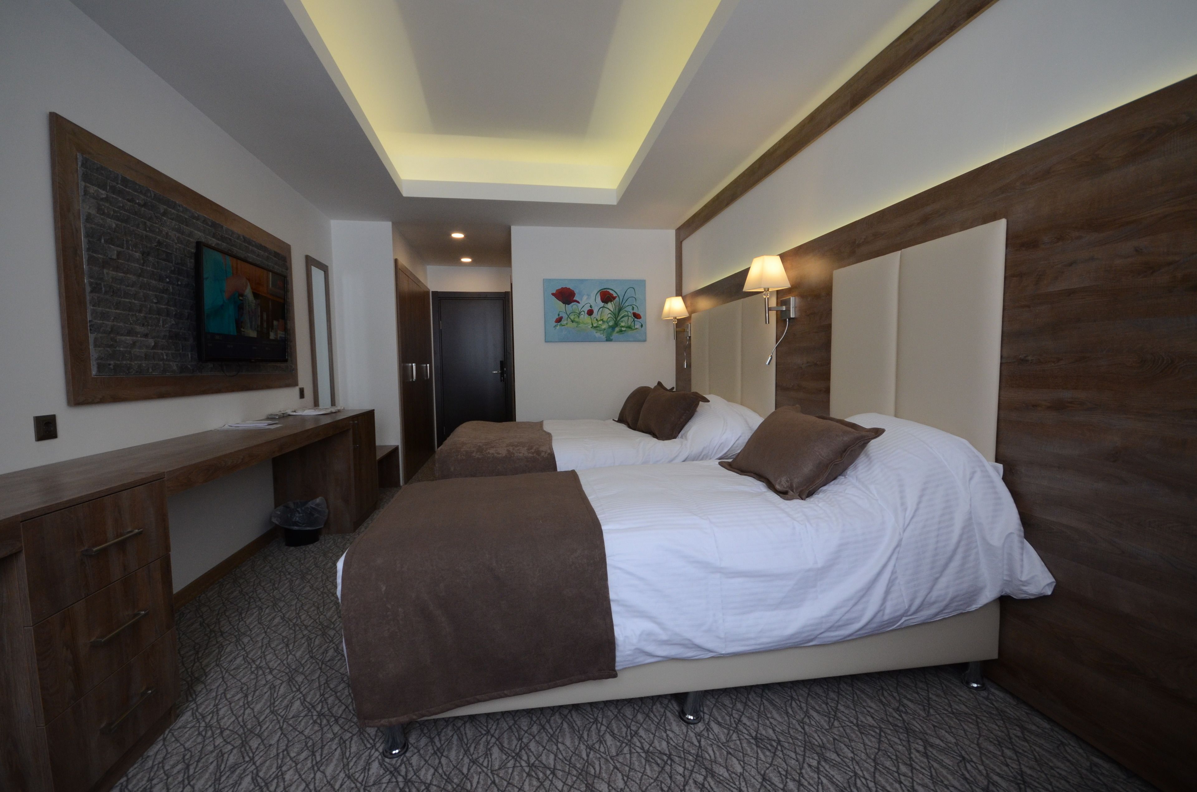 A hotel room with two beds, a desk, and a painting on the wall.