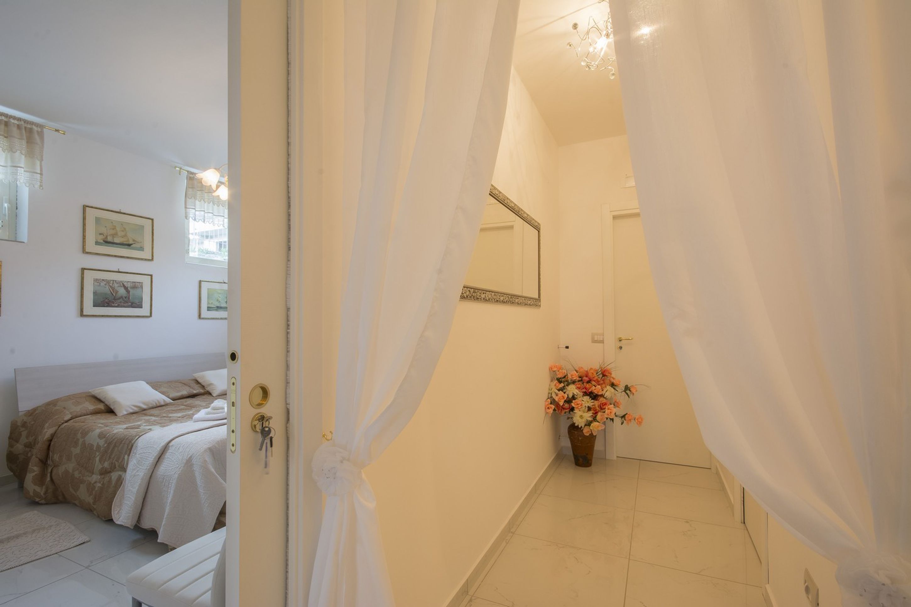 A bedroom with a bed, a bedside table, a mirror, and a vase with flowers.
