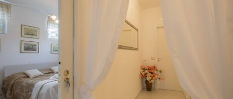 A bedroom with a bed, a bedside table, a mirror, and a vase with flowers.