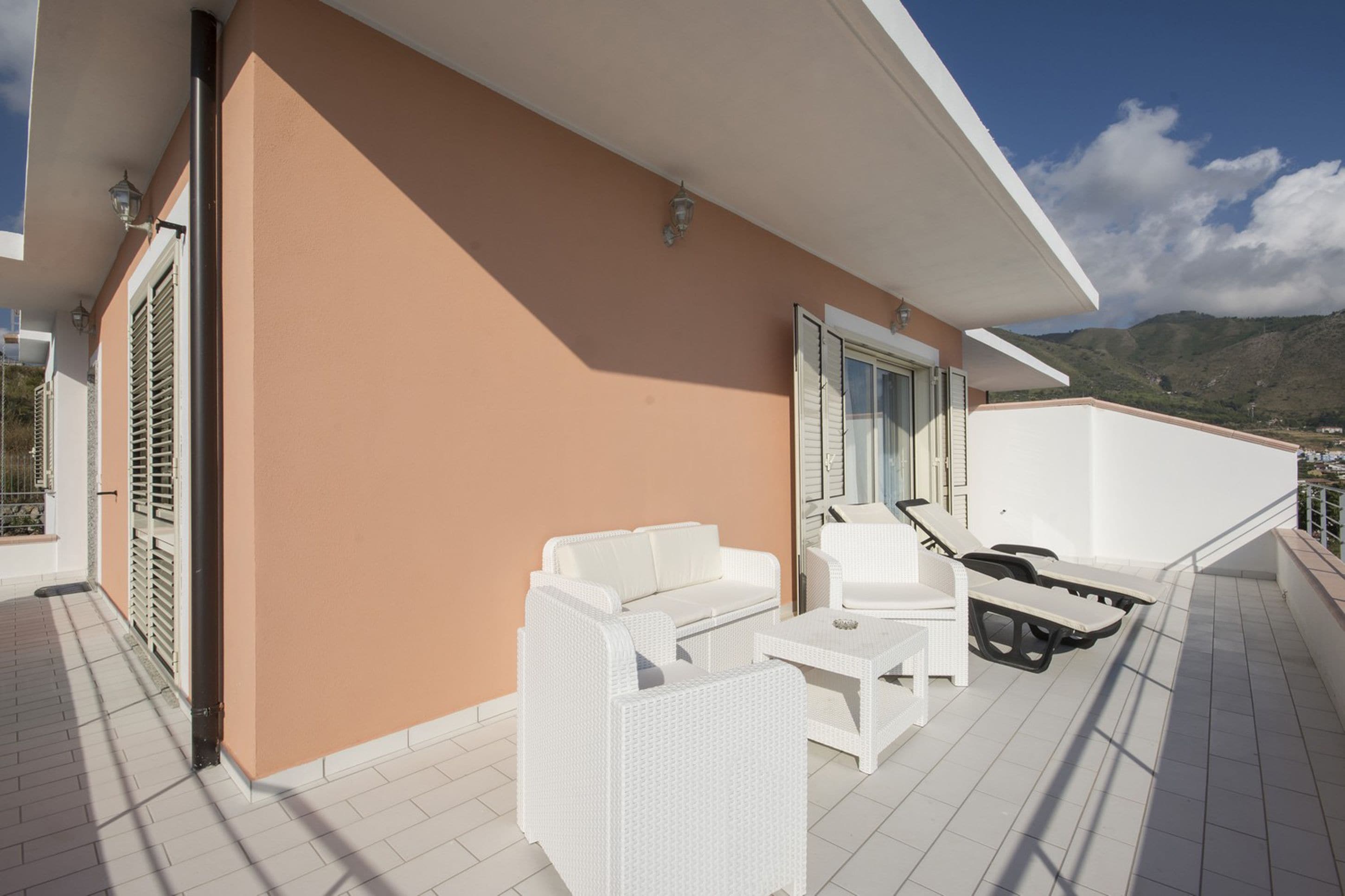 A balcony with white wicker furniture, including a sofa, chairs, and a table.
