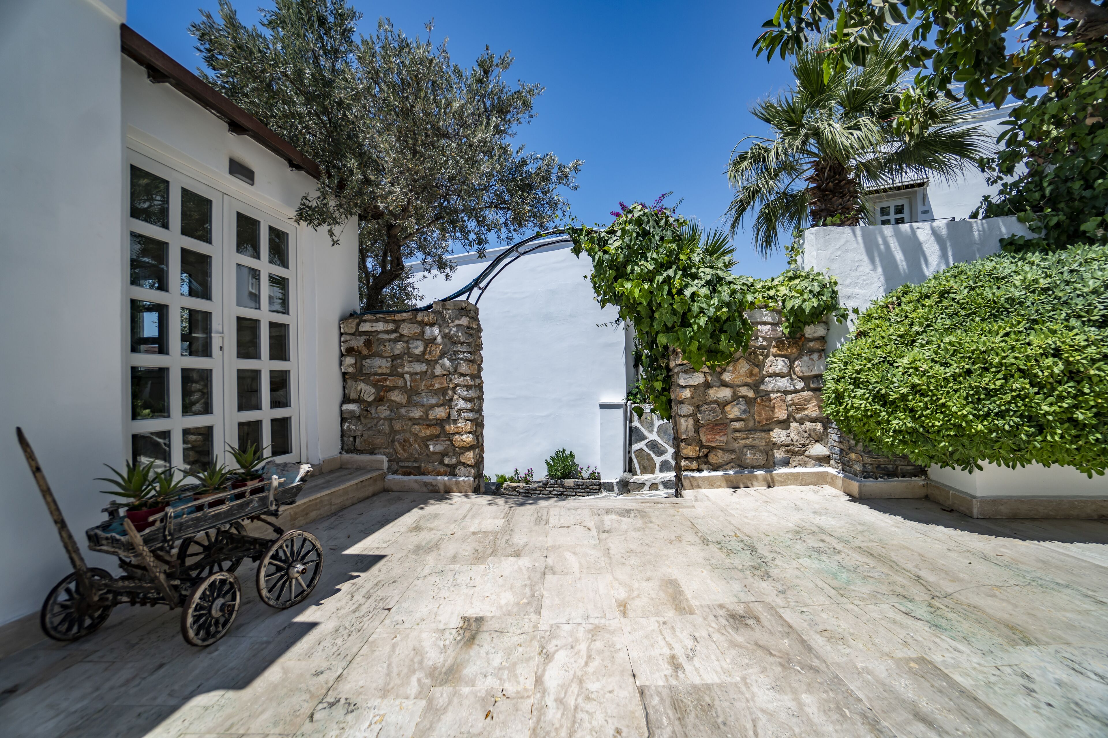A courtyard with stone walls, a wooden cart, and potted plants.