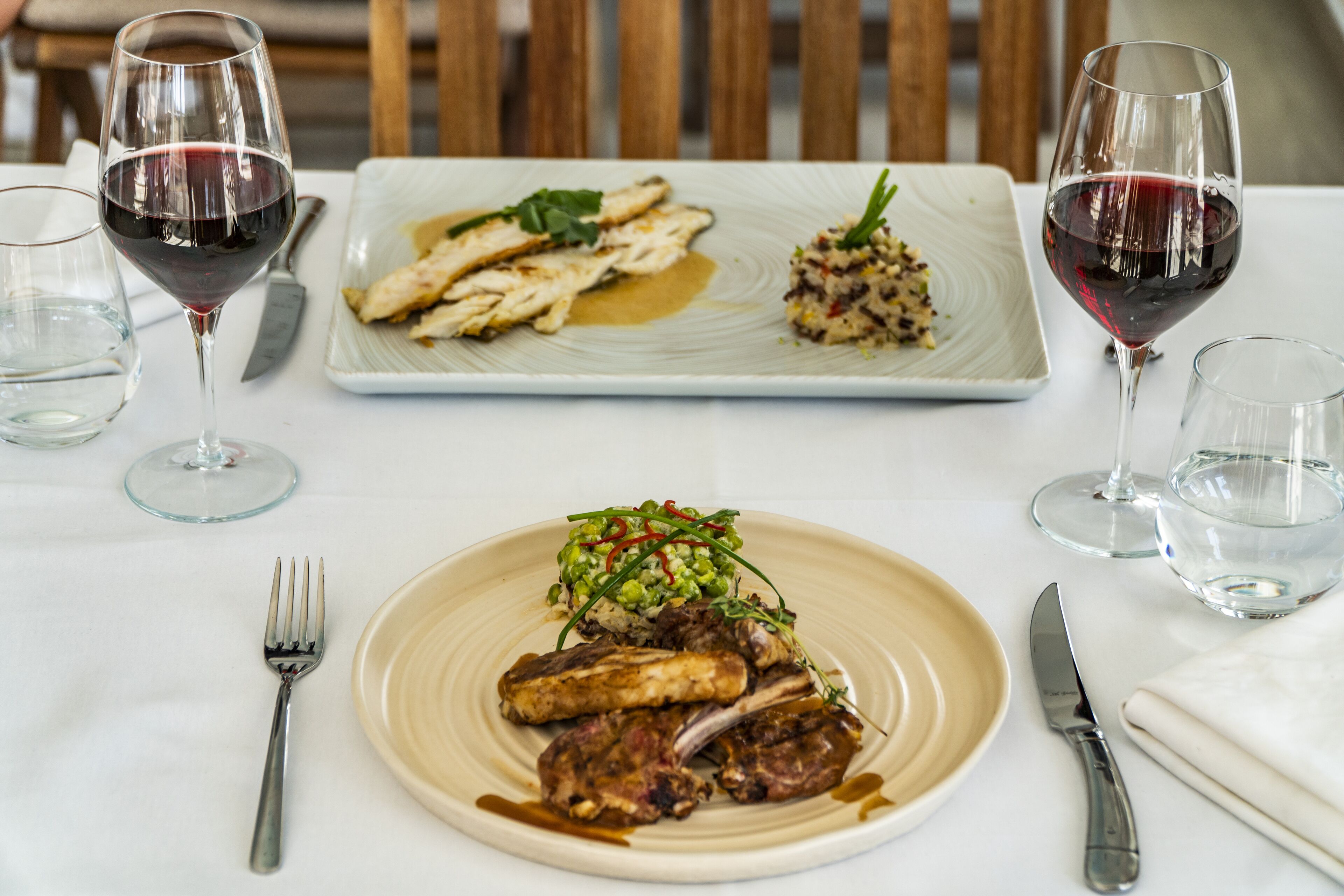 A dining table with plates of food, wine glasses, and cutlery.
