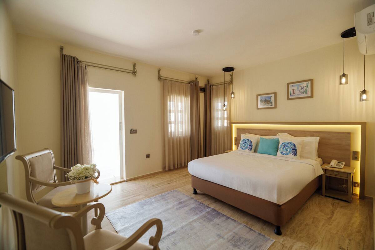 Habitación de hotel con cama, escritorio, silla, pequeña mesa con un florero y mesita de noche con teléfono.