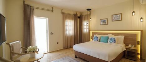 A hotel room with a bed, a desk, a chair, a small table with a flower vase, and a nightstand with a phone.