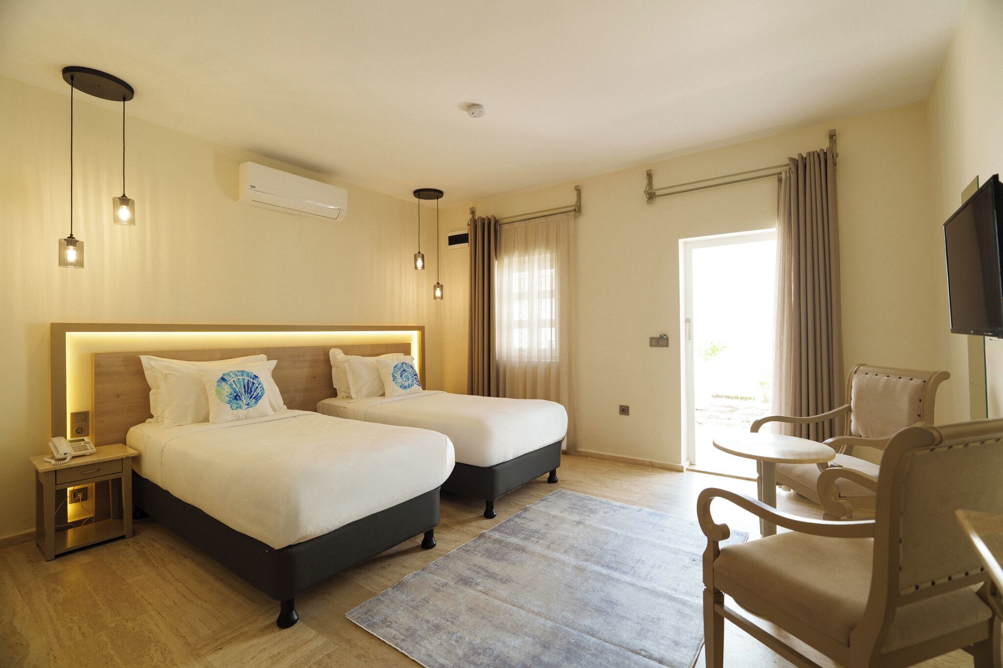 Une chambre d’hôtel avec deux lits, un bureau, une chaise, une télévision et une fenêtre avec des rideaux.