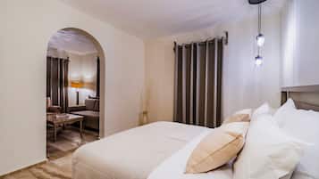 A hotel room with a large bed, a desk, and a chair. There is a lamp on the desk and a curtain on the window.
