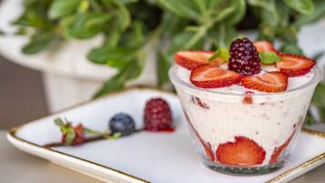 En dessert i et glas med jordbær og brombær ovenpå, placeret på en hvid tallerken med guld kant.