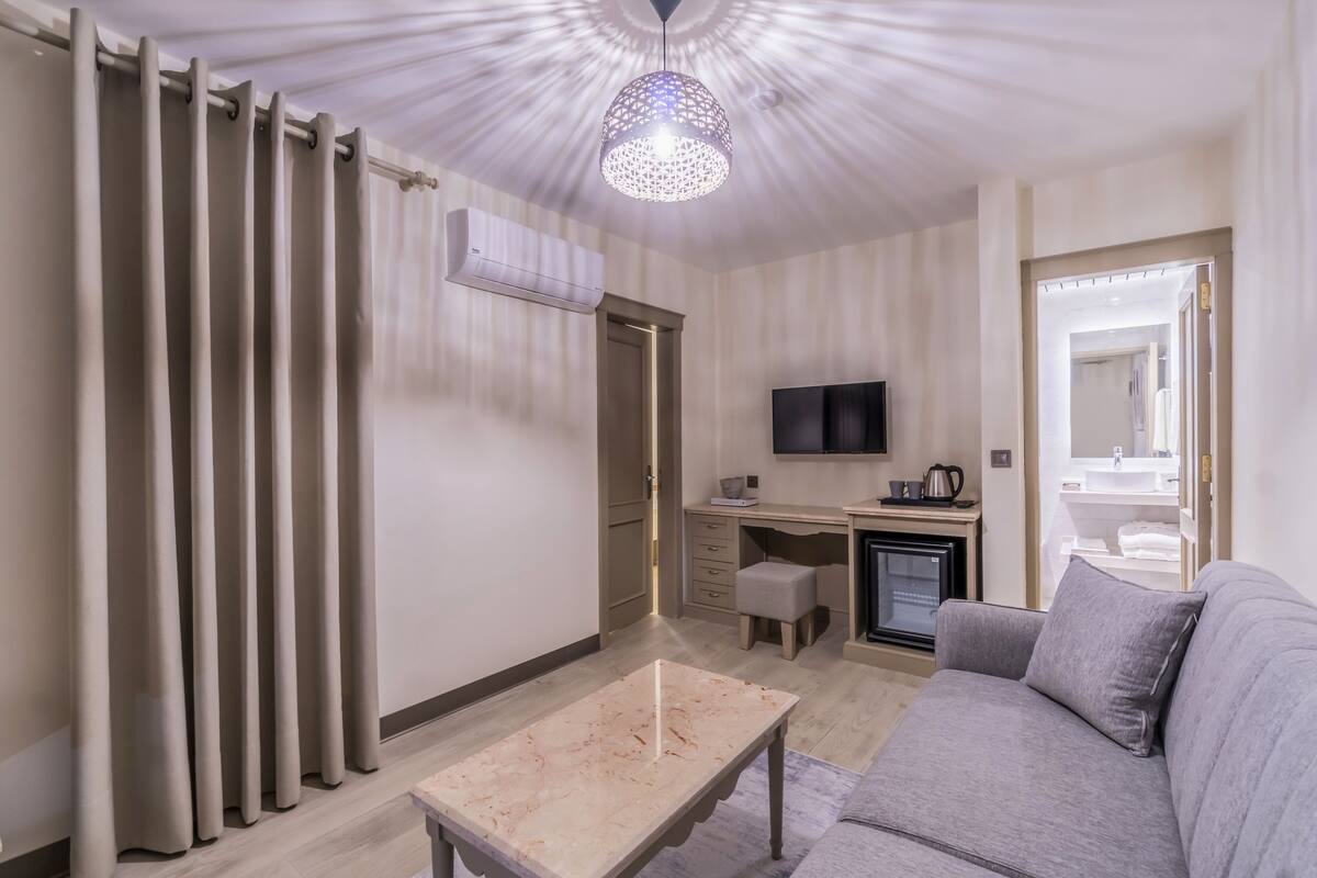 Una habitación moderna con sofá, escritorio, televisión y un baño visible a través de una puerta abierta.