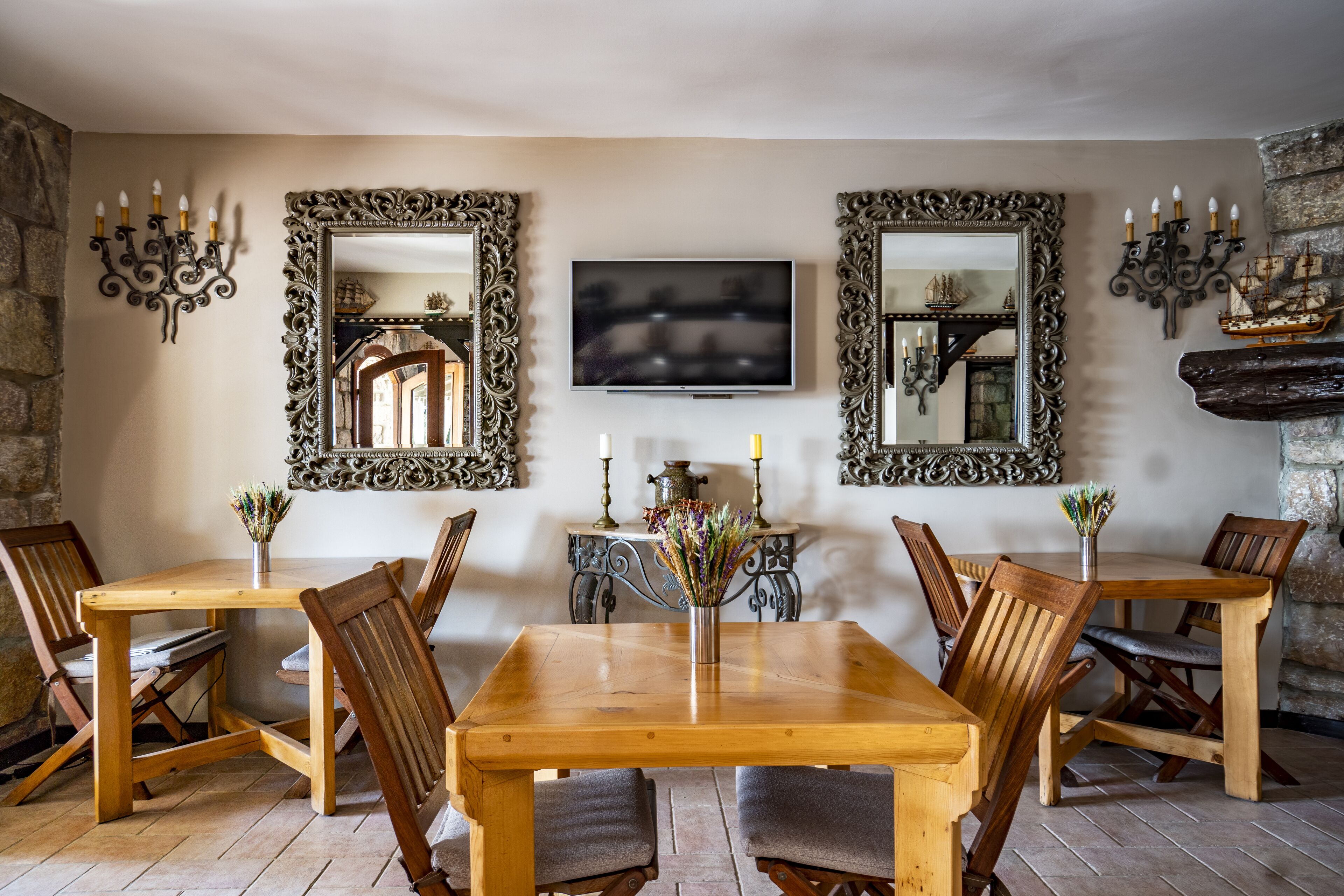 Uma sala de jantar com mesa e cadeiras de madeira, espelhos decorados, uma TV de tela plana e arandelas ornamentais.