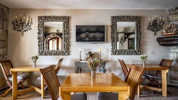 Uma sala de jantar com mesa e cadeiras de madeira, espelhos decorados, uma TV de tela plana e arandelas ornamentais.