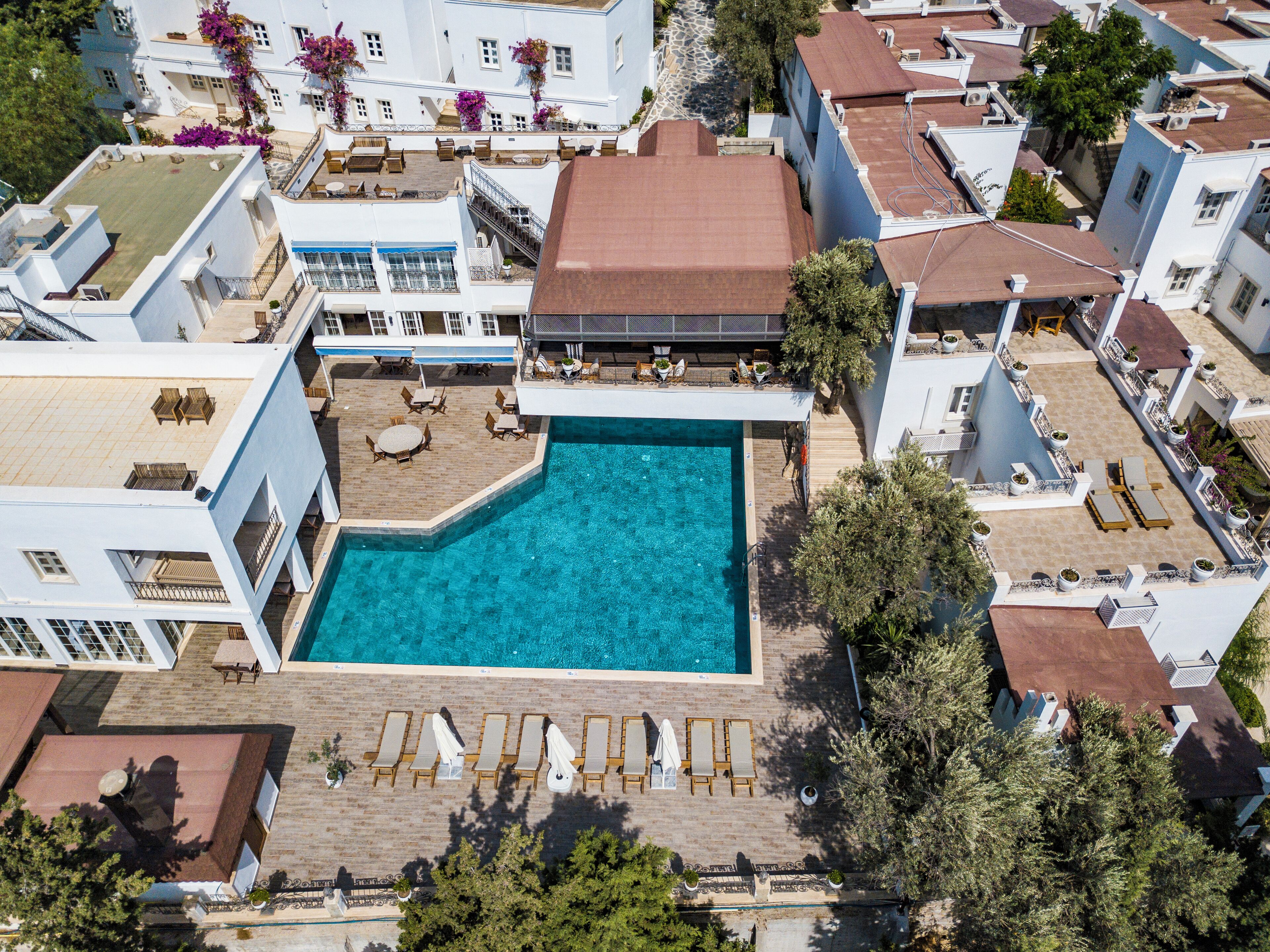 An aerial view of a hotel with a central swimming pool, multiple balconies, and outdoor seating areas.