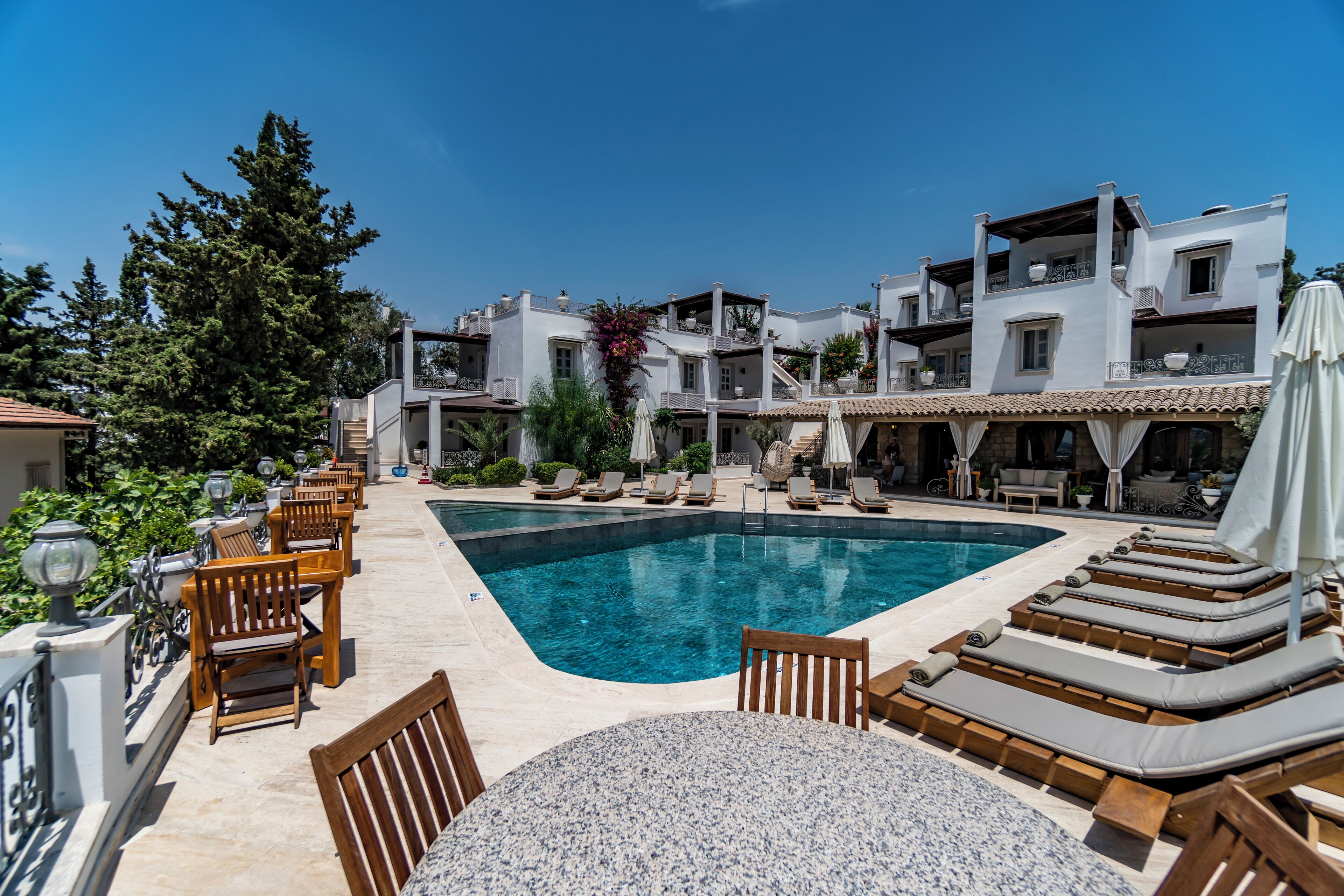 A poolside area with lounge chairs and a table, surrounded by white buildings with balconies.