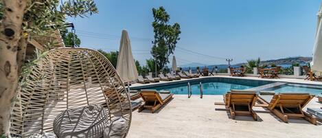 A poolside area with lounge chairs, a wicker chair, and umbrellas.