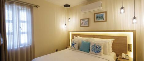 A hotel room with a large bed, a bedside table with a phone, and a wall-mounted air conditioner.