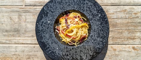A black bowl with spaghetti and a slice of yellow bell pepper on a wooden surface.