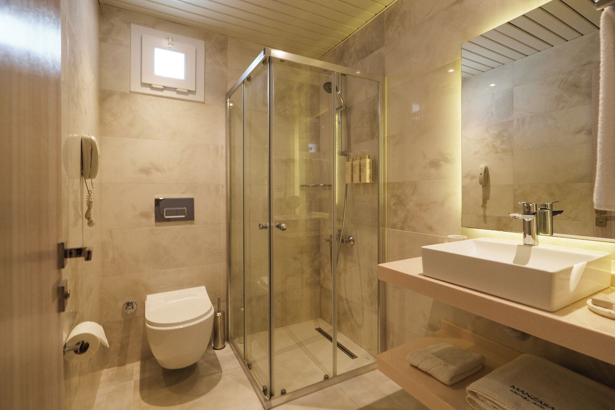 Un baño moderno con ducha de vidrio, lavamanos blanco y retrete.
