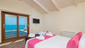 A hotel room with a bed, a TV, a view of the sea, and a sliding door to the outside. - Orient Villas (Zakynthos)