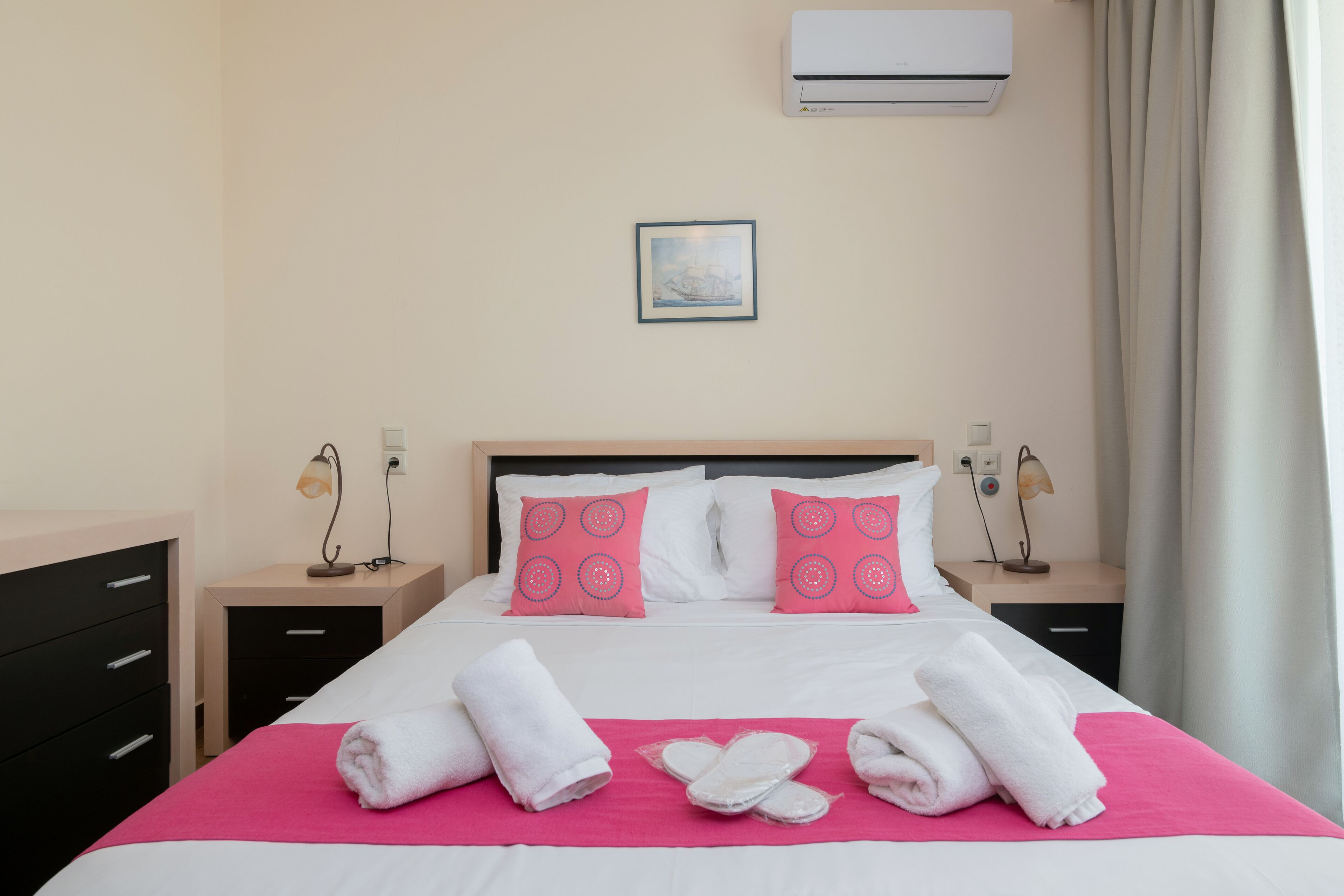 A hotel room with a bed, two nightstands, a wall-mounted air conditioner, and a window with curtains.