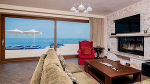A living room with a large sliding glass door leading to a beach view, a red armchair, a wooden coffee table, and a stone fireplace. - Orient Villas (Zakynthos)