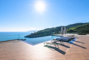 A rooftop infinity pool with a clear view of the sea, lounge chairs, and umbrellas. - Orient Villas (Zakynthos)